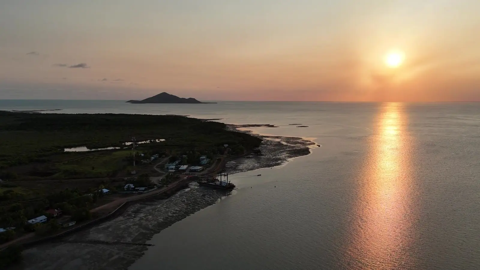 Aerial view of the Saibai Island shoreline at sunset, with the sun low over calm water