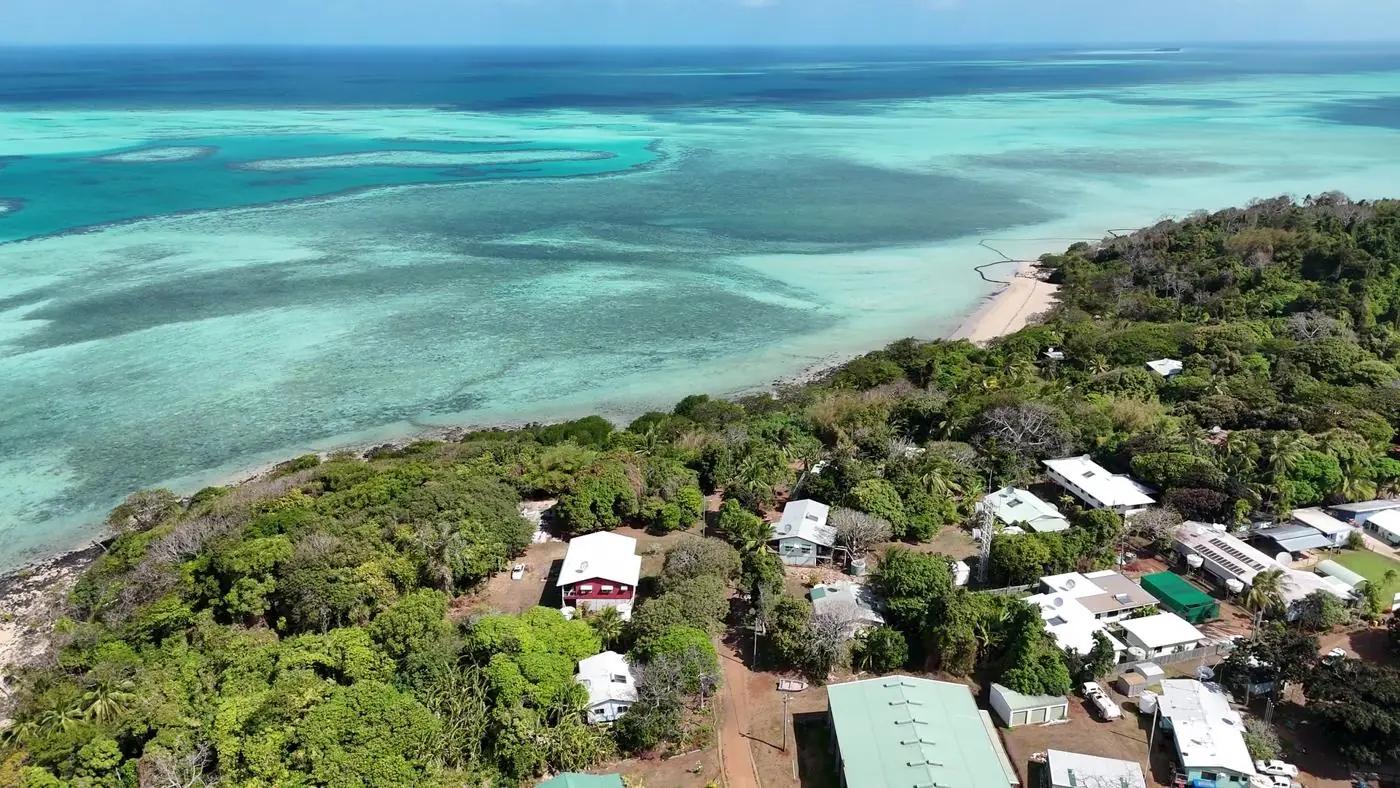 Aerial view of Ugar, a small Torres Strait island, with houses among trees beside reef flats and turquoise water