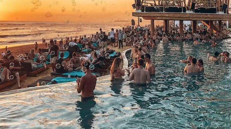 A crowded infinity-pool beach club in Bali at sunset, packed with tourists