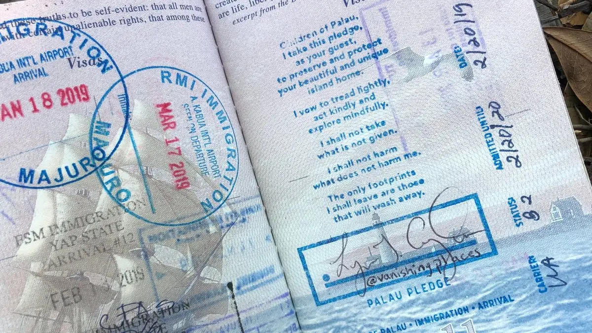 An open passport showing the Palau Pledge stamp, a commitment by the visitor to tread lightly, signed alongside arrival stamps from Palau, the Marshall Islands and Yap