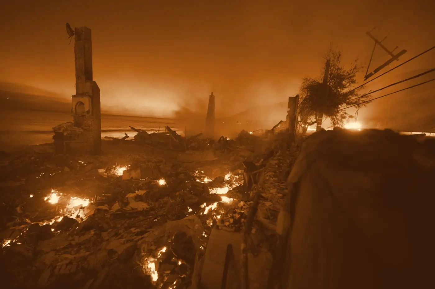 The aftermath of a wildfire, with burnt-out structures and smouldering rubble at dusk